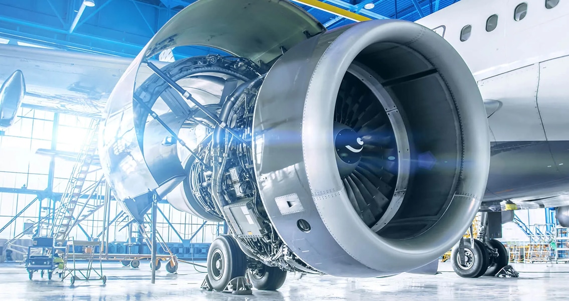 A close-up of a large airplane engine in a bright hangar, showing intricate details of the turbine and surrounding mechanical components. The image conveys precision and engineering excellence.