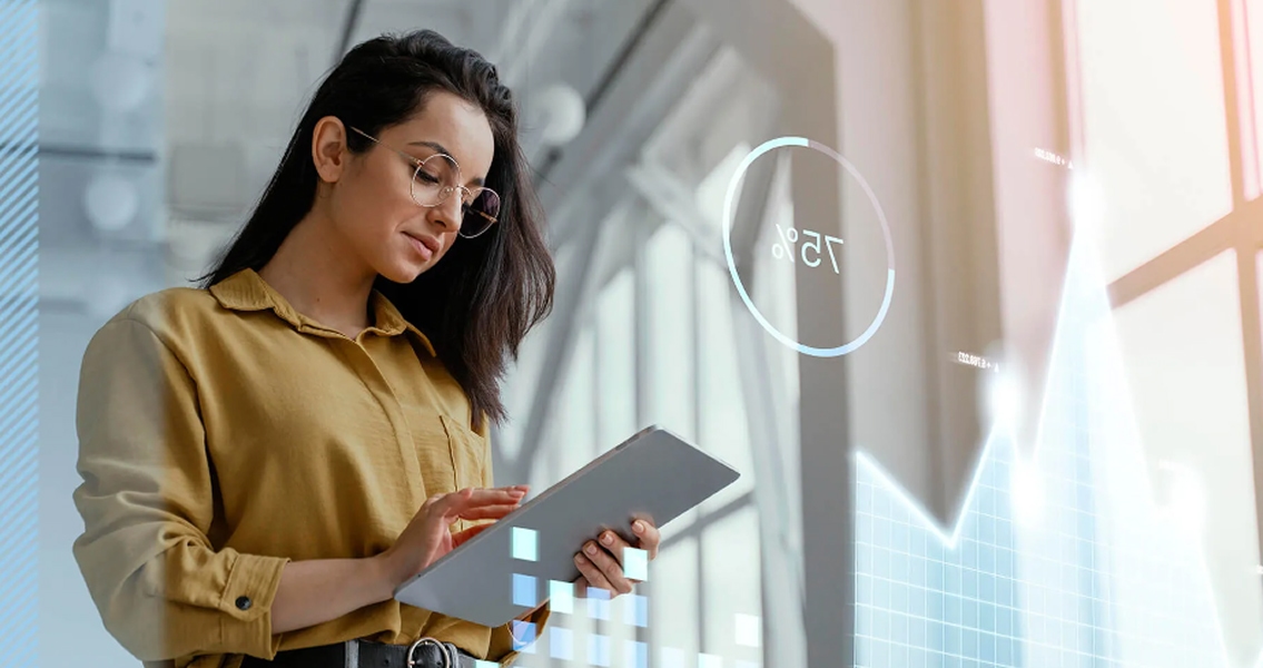 A woman in a mustard shirt and glasses holds a tablet, interacting with digital graphs and a 75% indicator. The scene conveys focus and technology.