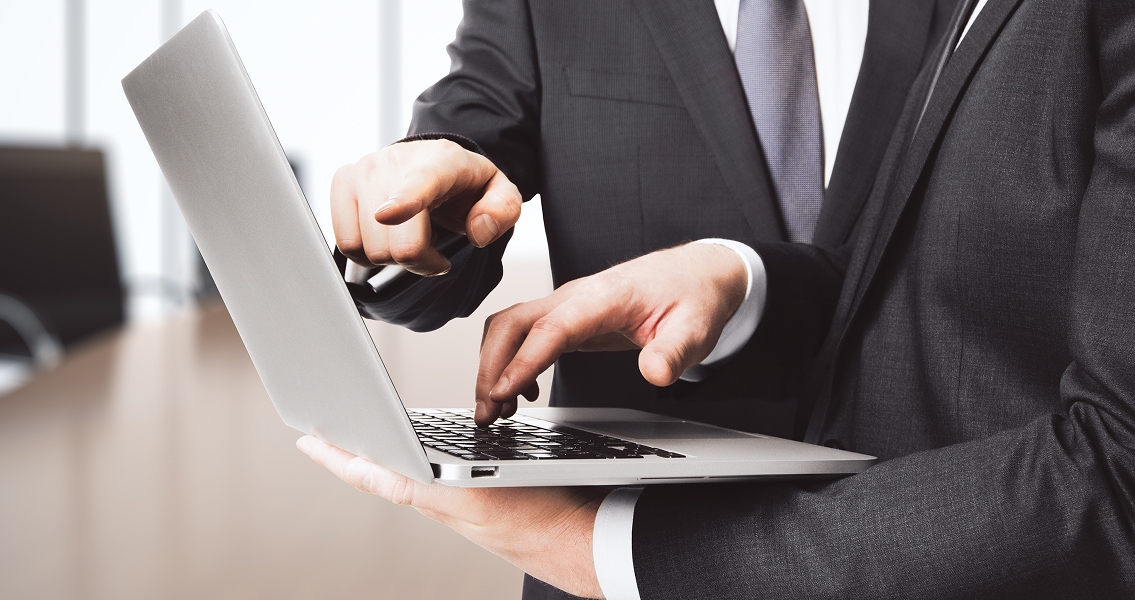 Two people in suits collaborate over a laptop, one typing while the other points at the screen in a modern office, conveying teamwork and focus.