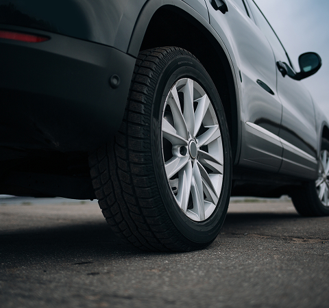 Close-up of a black SUV's rear tire on a paved road. The vehicle's sleek body and detailed wheel design convey a sense of durability and style.