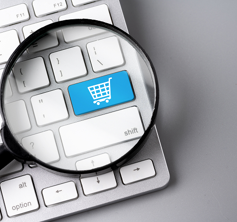 A magnifying glass focuses on a blue keyboard key displaying a white shopping cart icon, symbolizing online shopping and e-commerce exploration.
