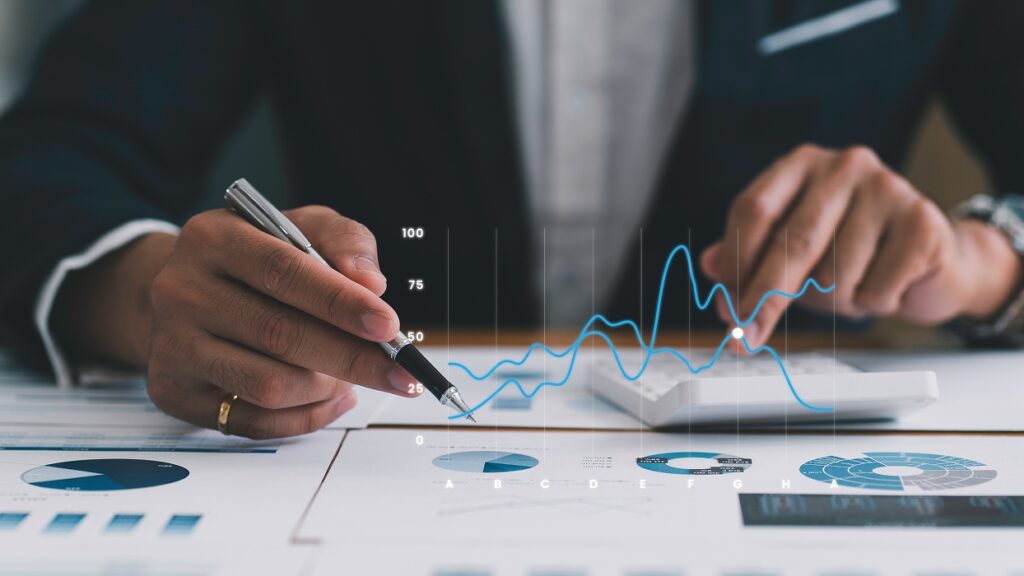 A person in a suit analyzes financial charts with a pen and calculator. Blue line graph and pie charts on paper signify detailed data assessment.