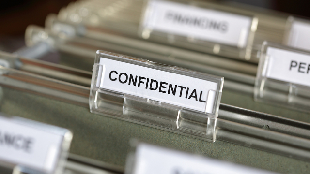 Close-up of a filing cabinet with a clear tab labeled "Confidential" in focus, flanked by other labeled tabs. The tone is professional and secretive.